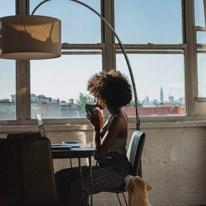 woman sipping tea at laptop with large windows