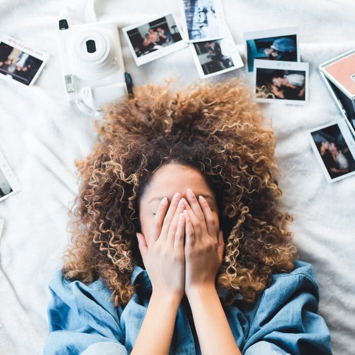 woman laying in bed surrounded by photos covering eyes