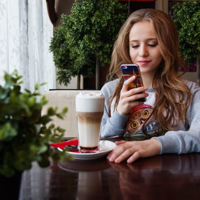 woman with iced coffee, smiling at mobile device