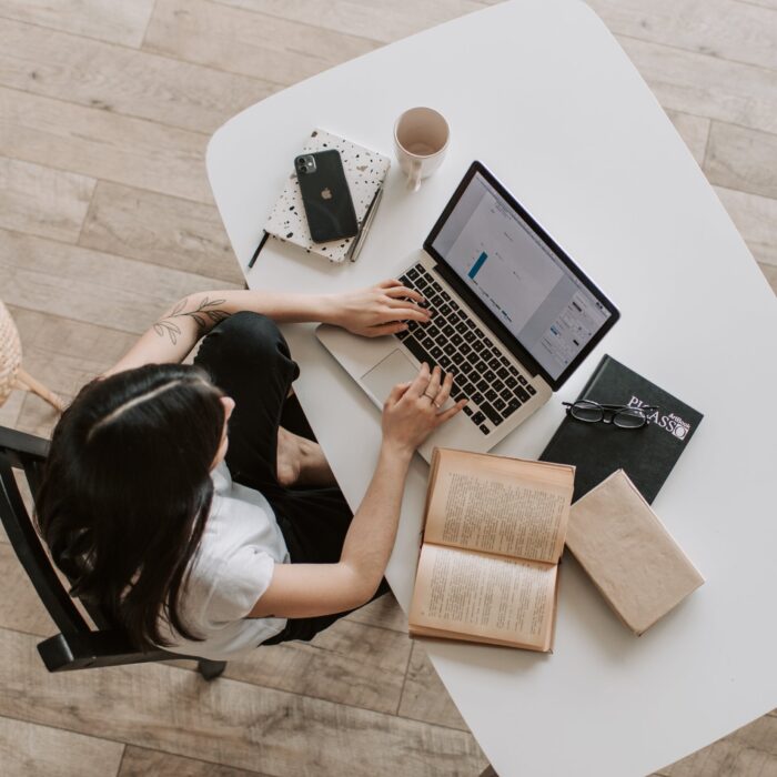 woman on her laptop working at a desk with books phone coffee mug