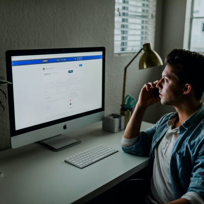 man looking at a desktop computer talking on the phone