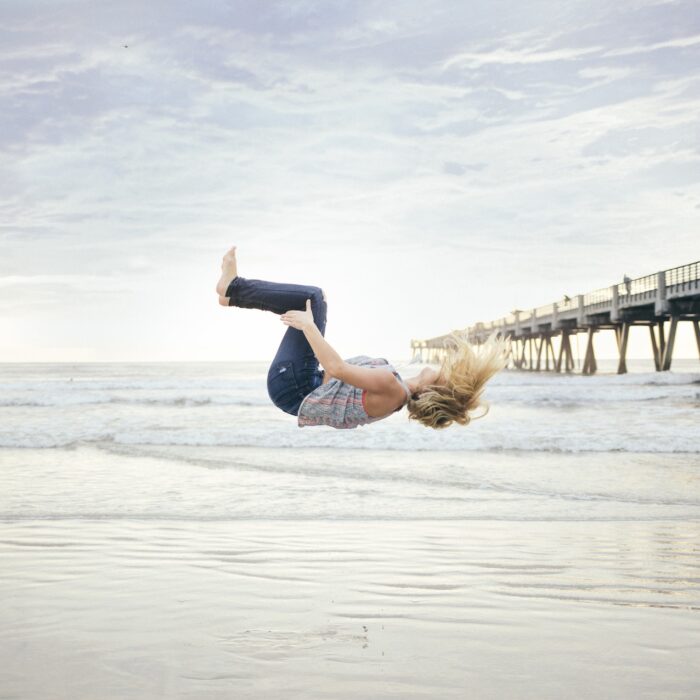 woman doing a backflip off a dock at beach