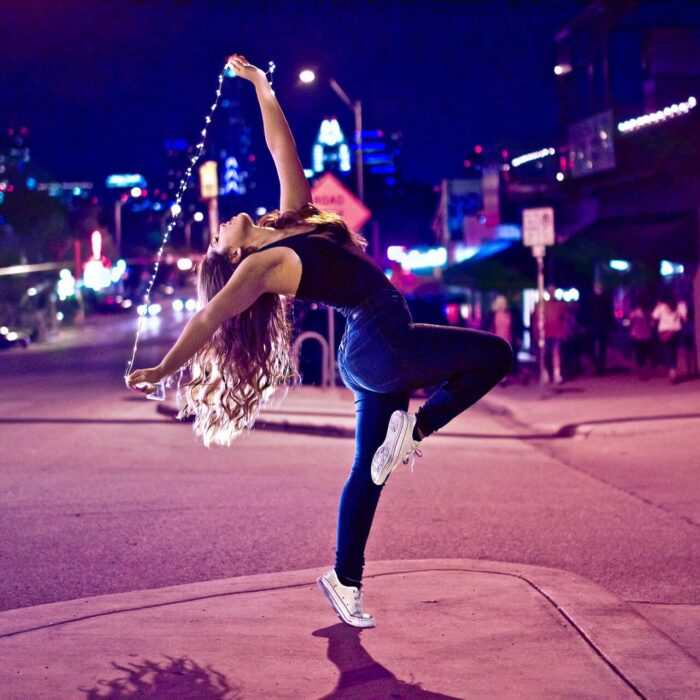 woman dancing in the street with a string of lights