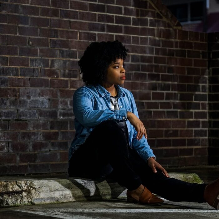 woman sitting in parking lot with brick wall behind her