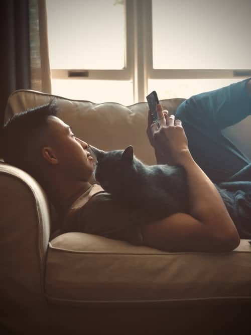 man lying on couch holding cat and phone