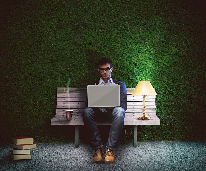 man on laptop sitting on bench in front of hedge