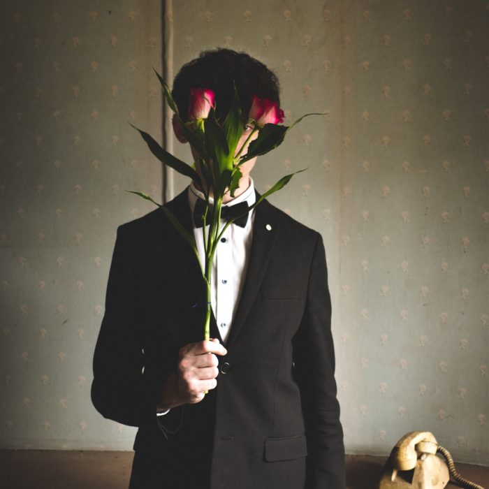 man in suit hiding his face behind flowers