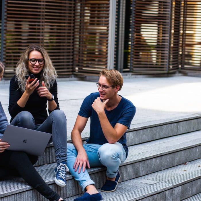 three friends sitting on steps with laptop