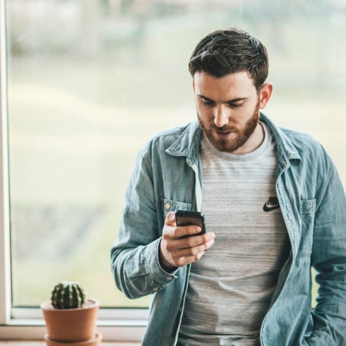 man browsing phone next to cactus