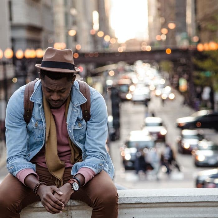 man in hat sitting on ledge over street