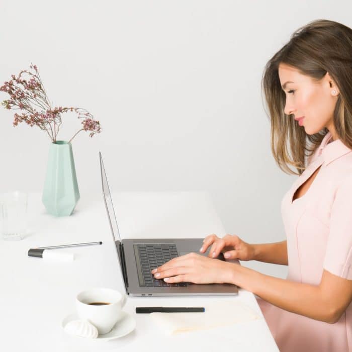 woman in pink on laptop standing with vase of flowers