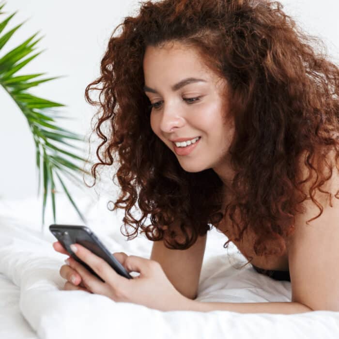 Woman in lingerie using phone in bed