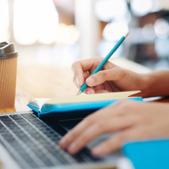 Hands writing on a planner while typing on a computer keyboard