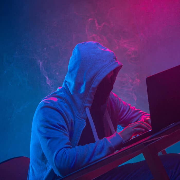 Hooded computer hacker stealing information with laptop