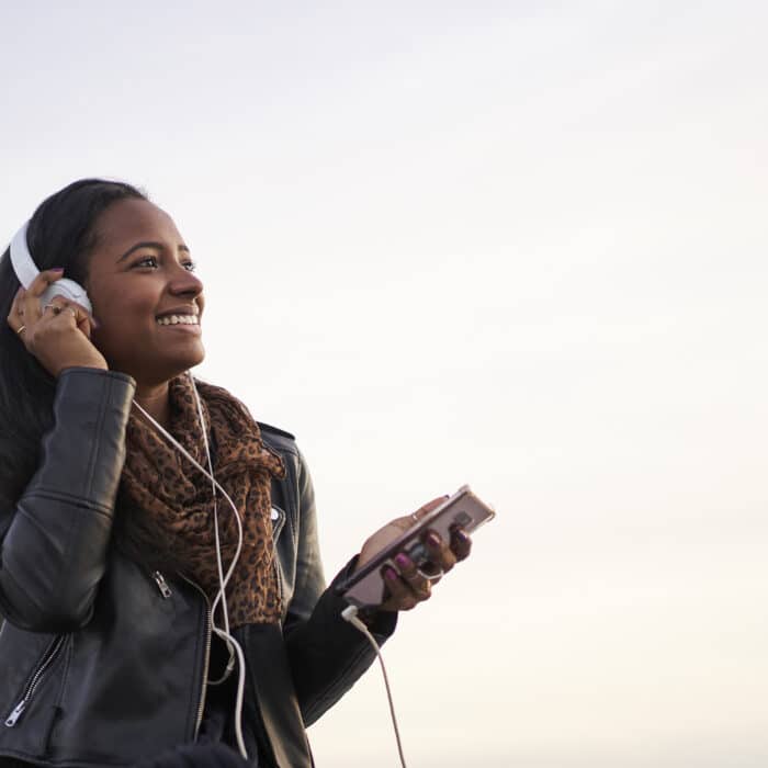 Panoramic shot of young African American woman with headphones listening to music outdoors. Isolated silhouette in the sky