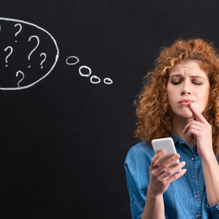 Pensive woman using smartphone, question marks in thought bubble on blackboard behind