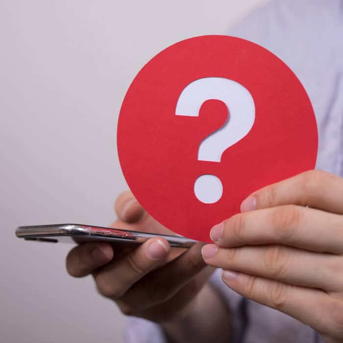 Sign of the question mark made of red paper and smartphone in the hands of a man
