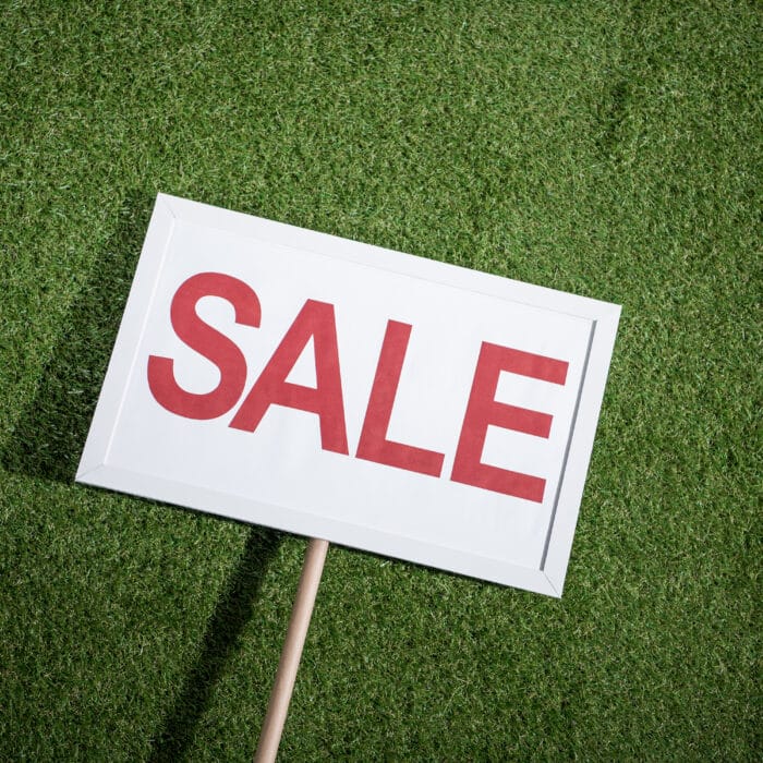 White sale banner lying on green grass, house for sale concept