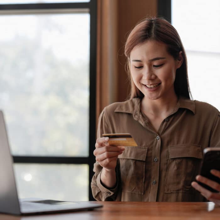 Young asian woman buying from online shop, using mobile phone and credit card, shopping from home.