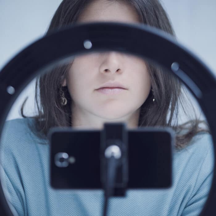 Young tiktoker creating videos for her followers using a smartphone, the ring light is covering her eyes